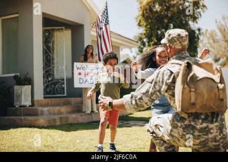 American soldier receiving a warm welcome from his family. Military man embracing his children after coming back home from the army. Serviceman reunit Stock Photo