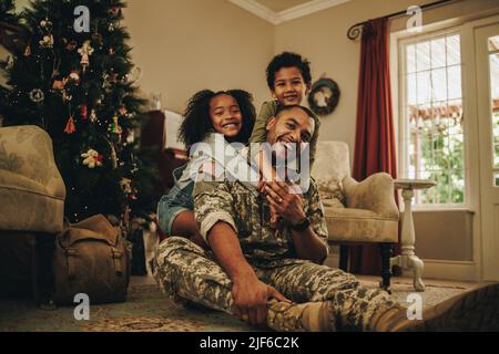Happy military family smiling joyfully while spending Christmas together. Cheerful military dad reuniting with his children at Christmas. Soldier spen Stock Photo