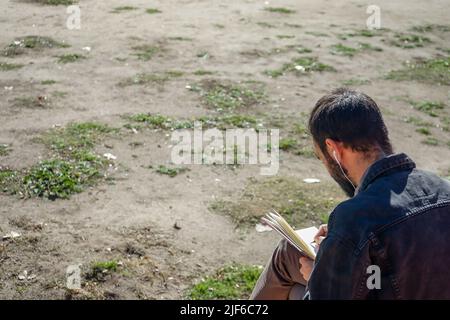 Man writing or drawing on notebook in a park. Stock Photo