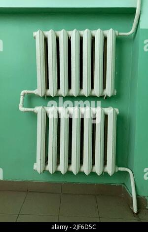 Old-fashioned cast iron water radiator with pipes in hallway or living room in soviet union style. Heating building home of winter. Vertical shot. Clo Stock Photo