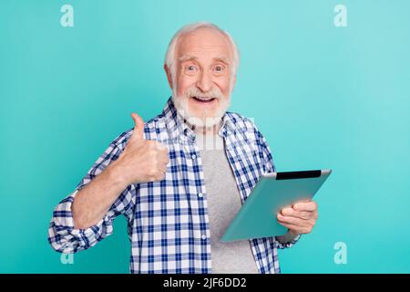 Photo of cheerful pensioner man in plaid shirt recommend you tablet modern technology device isolated on teal color background Stock Photo