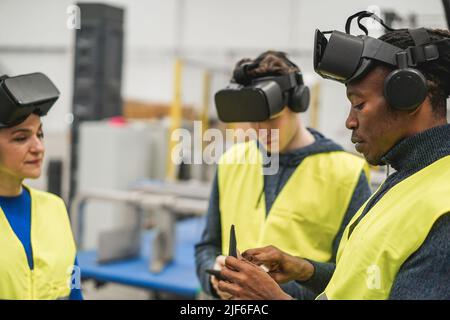 Multiethnic engineers using virtual reality glasses inside robotic factory - Focus on african man hand Stock Photo