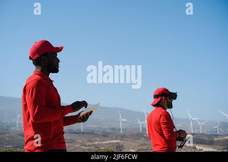 Engineers using virtual reality headset while working at windmill farm with tablet and drone - Focus on african man face Stock Photo