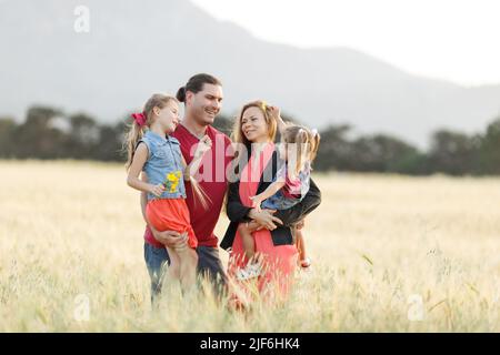 Happy family father of mother and two daughters sisters on nature at sunset.Carefree parents having fun with their kids on a field. Stock Photo