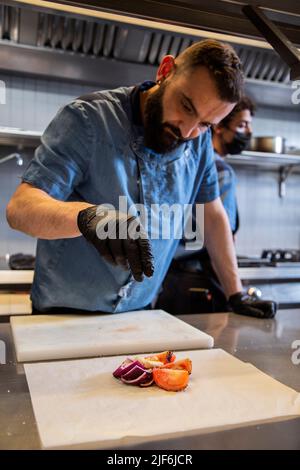 Chef sprinkling seasoning on food at counter in commercial kitchen Stock Photo