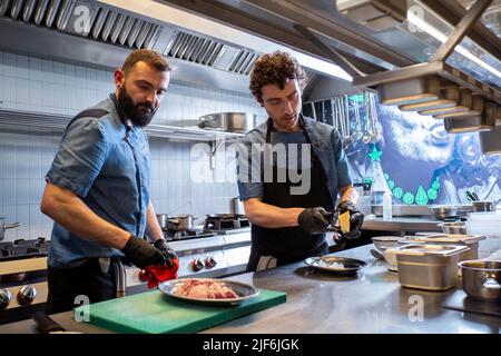 Caucasian chefs preparing dish for customer in commercial kitchen Stock Photo