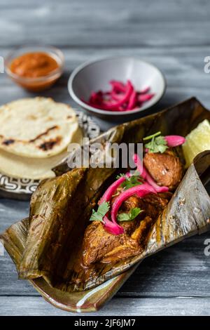 From above traditional Mexican cochinita pibil dish made of pork wrapped in banana leaf garnished with pickled onion and cilantro and served on cerami Stock Photo