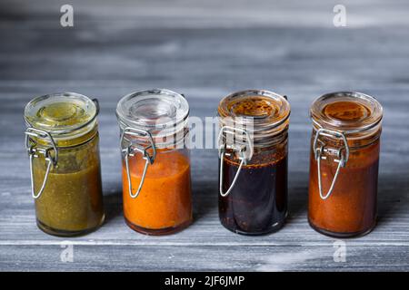 Closeup green salsa with jalapeno and avocado and habanero tatemado sauces in small glass jars placed near salsa macha with sesame and smoked chipotle Stock Photo