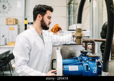 Focused male scientist in medical uniform tightening bolts with wrench on special machine with hose while working in modern light laboratory Stock Photo