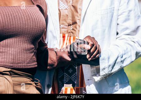 Unrecognizable African man and Woman in love in trendy clothes holding hands on sunny day Stock Photo