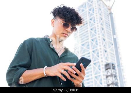 From below of young male in green shirt using modern mobile phone while walking on city street Stock Photo