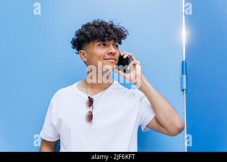Positive male on blue wall and talking on the phone on mobile phone Stock Photo