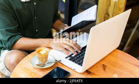 Anonymous ethnic male freelancer with coffee while working remotely on modern netbook in cafe Stock Photo