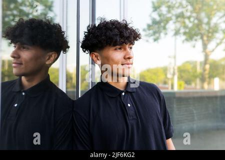Positive man in black polo leaning on window and gazing at green trees growing outside on serene summer day Stock Photo