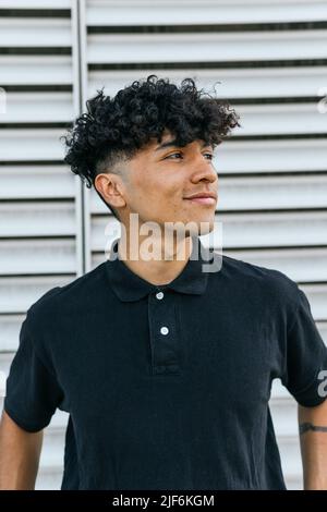 Positive man in black polo leaning on wall outside on serene summer day Stock Photo