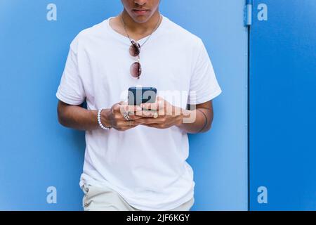 Anonymous male leaning on blue wall and typing text message on mobile phone Stock Photo