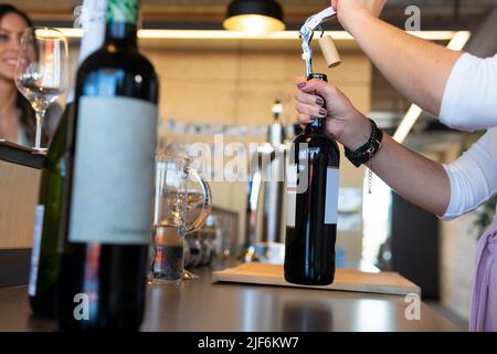 Soft focus of anonymous Woman using corkscrew for opening bottle at start of wine tasting procedure in restaurant Stock Photo