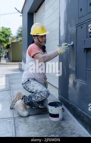 Side view of professional male painter in gloves painting wall using brush while sitting on sidewalk on city street Stock Photo