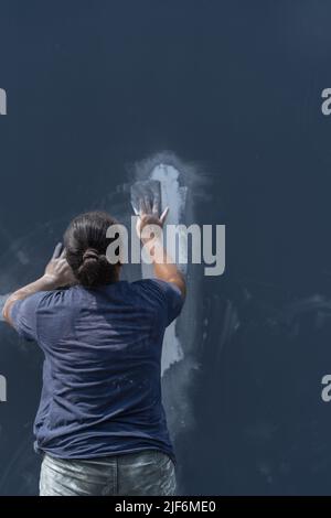 Side view of professional female painter in process of plastering wall using special equipment on city street Stock Photo