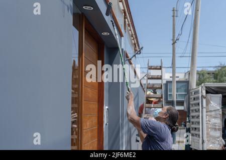 Side view of professional female painter in protective mask standing on sidewalk and painting wall using roller on city street Stock Photo