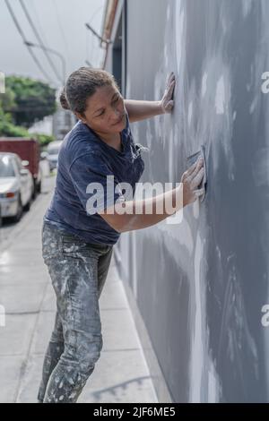 Side view of professional female painter in process of plastering wall using special equipment on city street Stock Photo