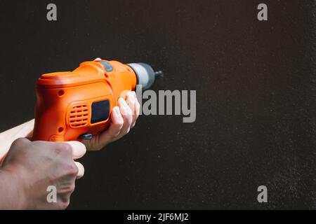 Hands of crop unrecognizable person making hole in black wall with professional electric drill in room with sunlight at home Stock Photo