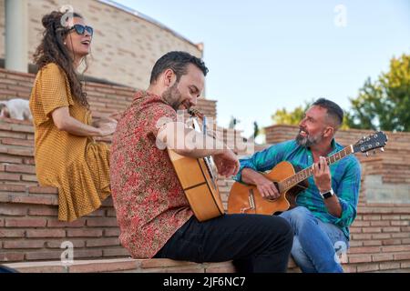 From below content male musicians playing songs on acoustic guitars while sitting on steps with dog and Woman on street Stock Photo