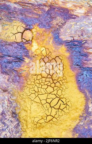 Abstract textured background of bright yellow and violet dry soil with cracks during drought Stock Photo
