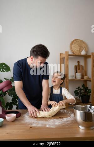 Smiling father and daughter holding dough near table at home Stock Photo