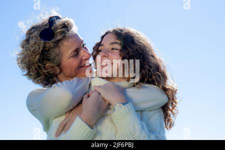 Closeup portrait of smiling mother embracing daughter on sunny day Stock Photo