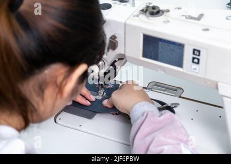 Anonymous cropped dressmaker in uniform sewing on machine while working at table with threads in workshop Stock Photo