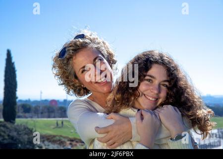 Closeup portrait of smiling mother embracing daughter on sunny day Stock Photo