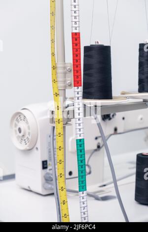 Soft focus of colorful long measuring tape hanging near spools of dark threads on professional machine during work in workshop Stock Photo