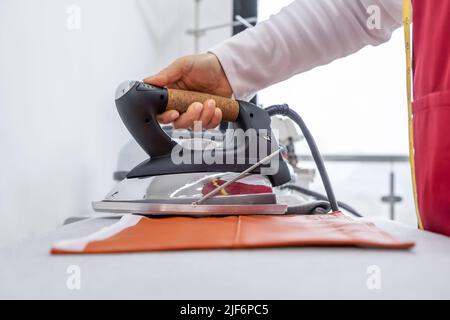 Crop anonymous professional seamstress with measuring tape ironing colorful textile on board while working in modern light atelier Stock Photo