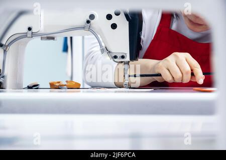 Crop unrecognizable seamstress in uniform using screwdriver and screwing foot in sewing machine during work in light atelier Stock Photo