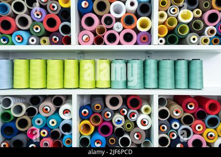 Set of colorful spools of threads for sewing stacked together on white shelves at wall in professional modern light atelier Stock Photo