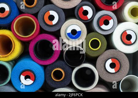 Set of colorful spools of threads for sewing stacked together on white shelves at wall in professional modern light atelier Stock Photo