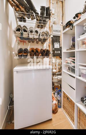 Modern white electric freezer under shelf near various shoes on storage Stock Photo