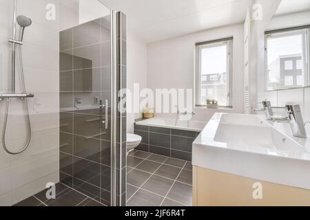 Sinks with mirrors and clean bathtub located near shower box with glass door in modern bathroom with white tiled walls Stock Photo