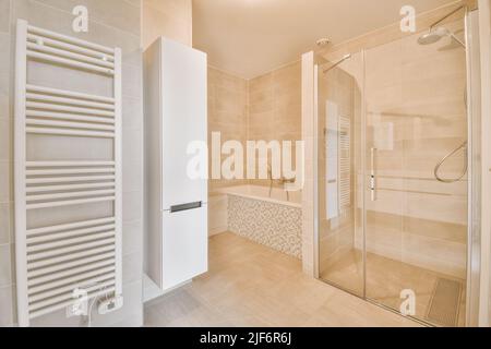 Bathtub located near shower box with glass door in modern bathroom with cabinet and radiator on tiled walls Stock Photo