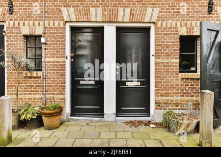 Exterior of modern residential house with brick walls tiled roof and decorative potted plants near entrance against cloudy blue sky in town Stock Photo