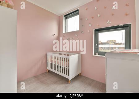 White baby crib and commode placed near window in cozy room with decorative butterflies on pink walls in modern apartment Stock Photo