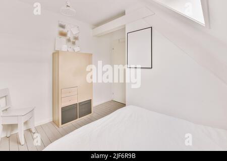 Wooden cabinet and chair in cozy bedroom with comfortable bed and empty frame in mansard Stock Photo