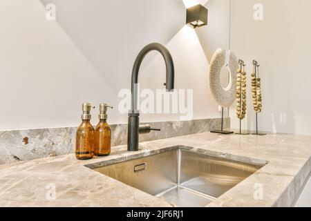 Sink with black faucet on marble gray counter with detergents under shining lamp in light modern kitchen of apartment Stock Photo