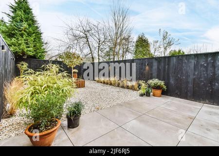 Terrace of house with tiled floor and pebble with abundance of potted green plants placed near wooden fence in countryside Stock Photo