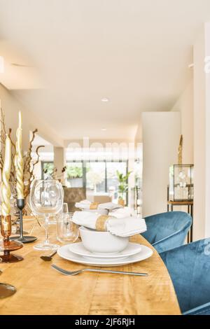 Tableware with cutlery served on wooden table with wineglasses and decorative candles in light stylish dining room in modern apartment Stock Photo