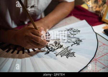 (220630) -- CHANGSHA, June 30, 2022 (Xinhua) -- A painter draws patterns on a fan at the Yueyang tower scenic spot in Yueyang City, central China's Hunan Province, June 23, 2022. Yuezhou fan dates back to the late Ming Dynasty (1368-1644) and early Qing Dynasty (1644-1911). The fan, having a history of about 400 years, is one of the most famous fans in China for its delicacy. Using fine bamboo as its framework, ox horn as the nail, and Xuan paper as the cover, the fan goes through 72 complicated procedures before done, while the making of framework requires most exquisite and skillful work. Th Stock Photo