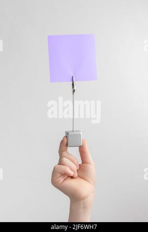 child hand holding purple blank reminder or paper notes above a white and gray background, copy space Stock Photo