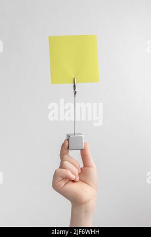 child hand holding yellow blank reminder or paper notes above a white and gray background, copy space Stock Photo