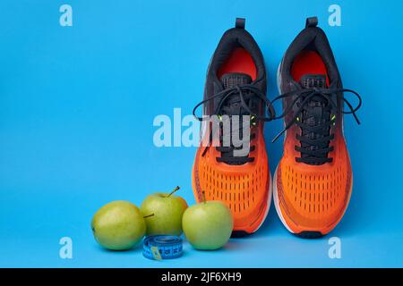 Orange sneakers, measuring tape and fruits green apples on a blue background Stock Photo